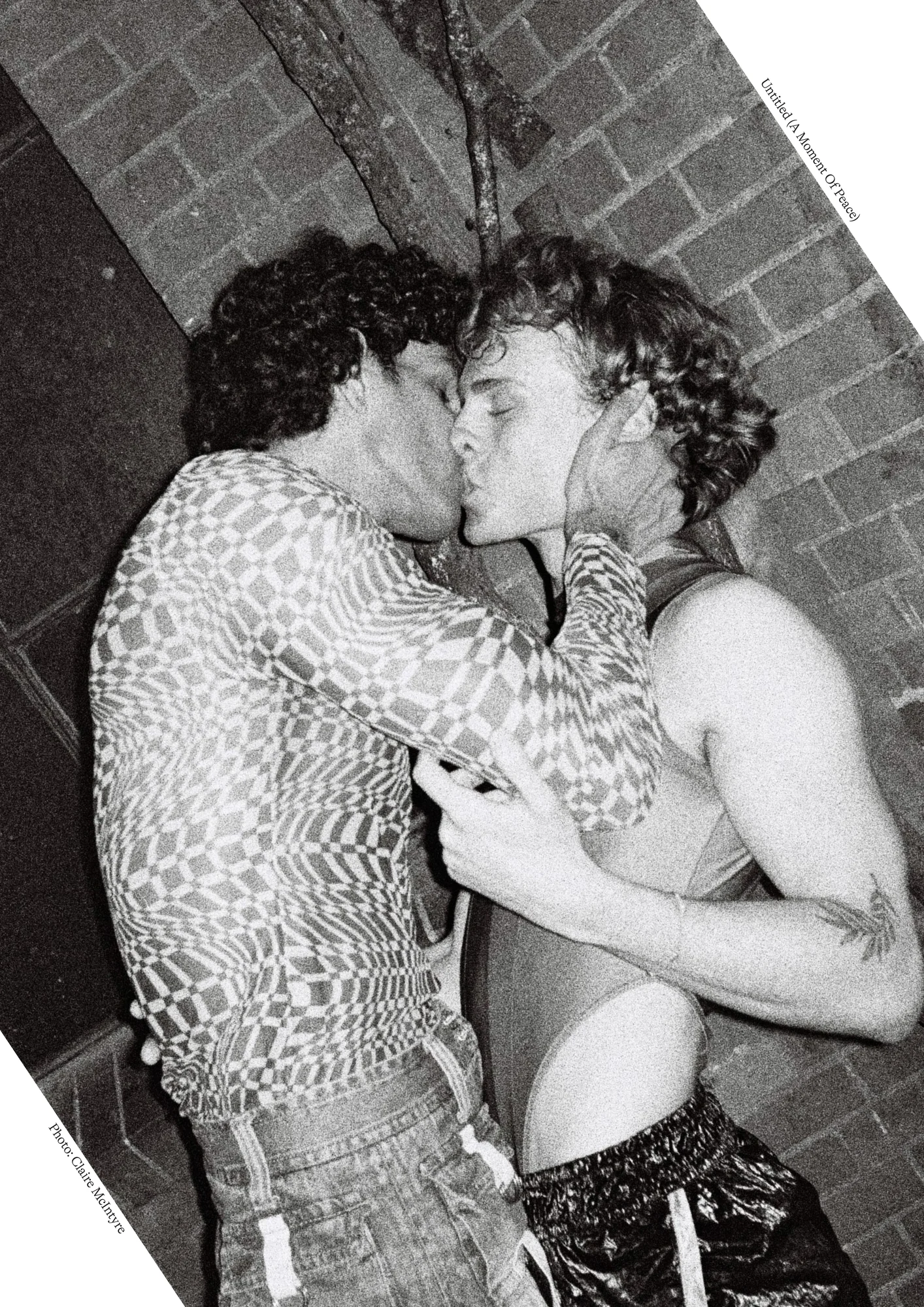 Black and white photo of two men kissing against a brick wall